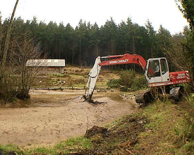 Sediment deposited by flood waters is removed from a pond.